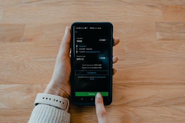 A caucasian person holding a smart phone in their left hand while looking at some monetary figures.