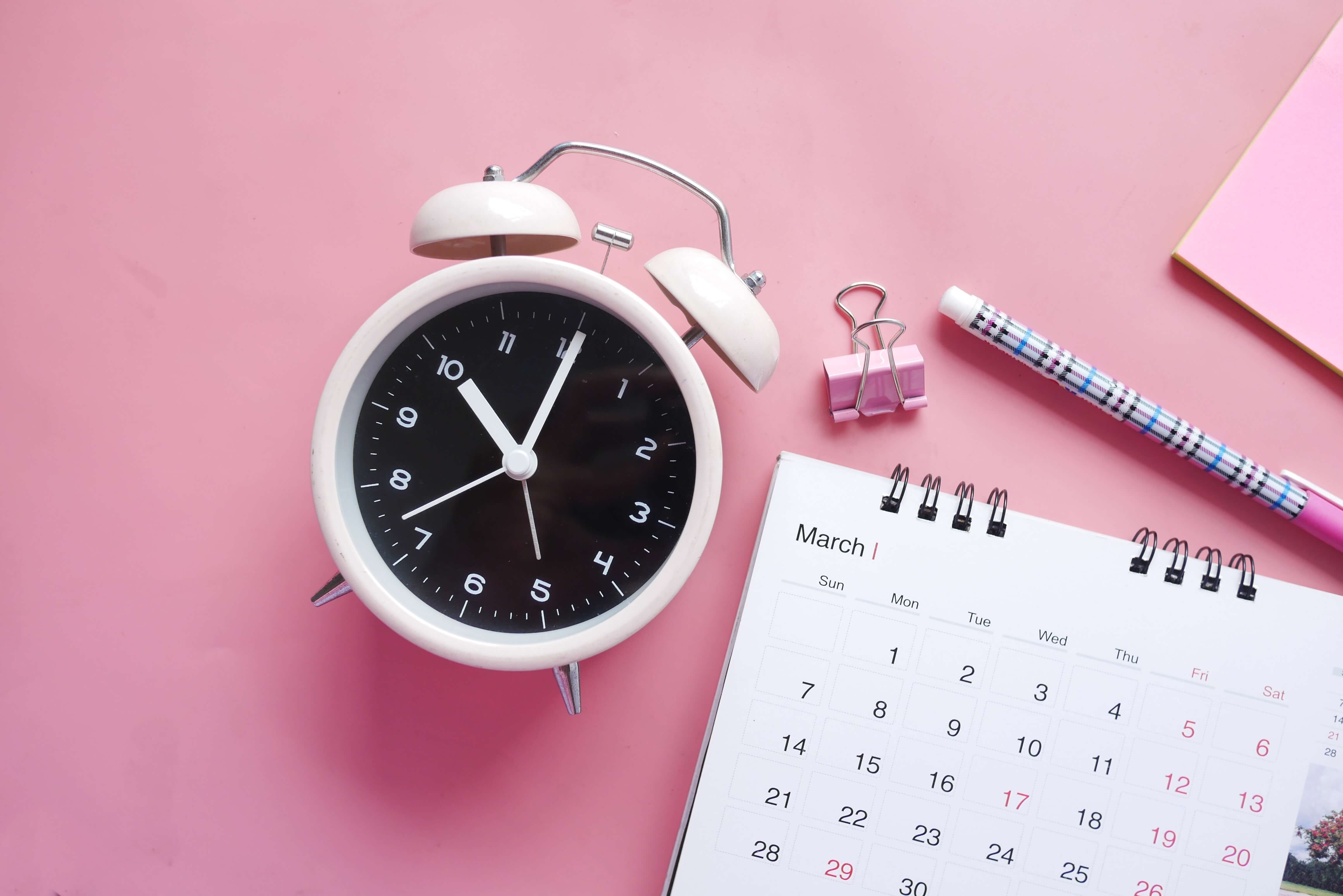 A calendar and alarm clock on a pink background