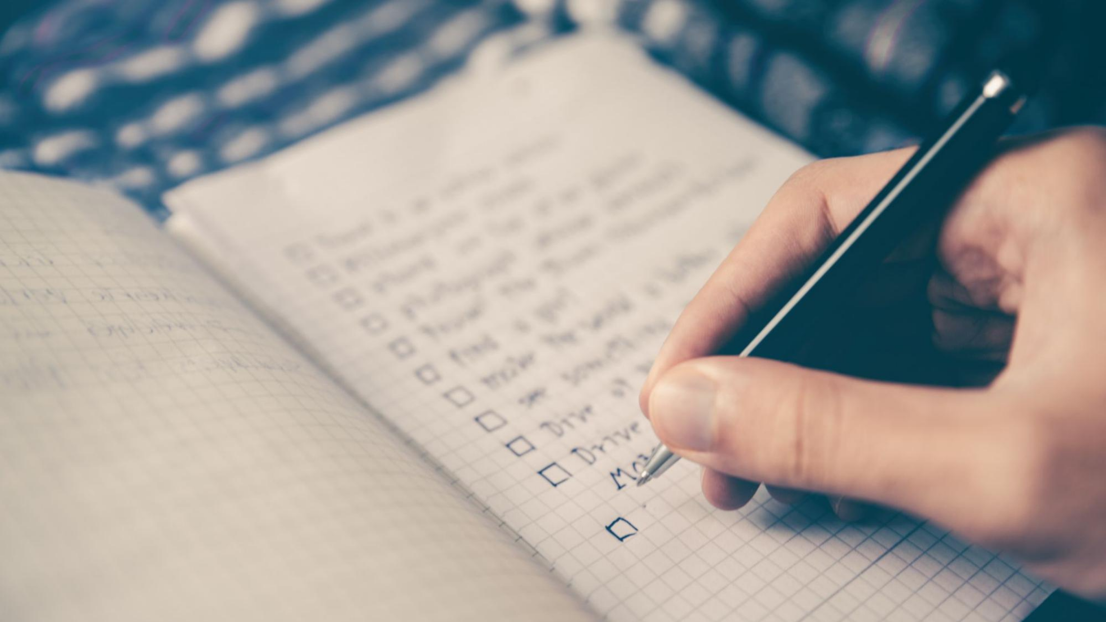 Hand holding a pen, writing a checklist on grid paper