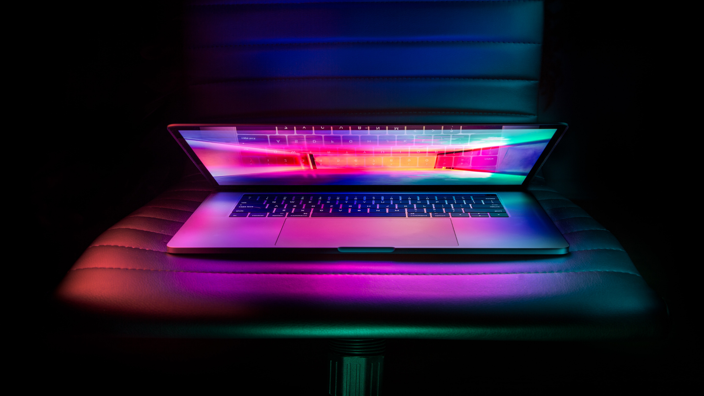 A laptop that's only partially open and has colorful lights coming from the screen