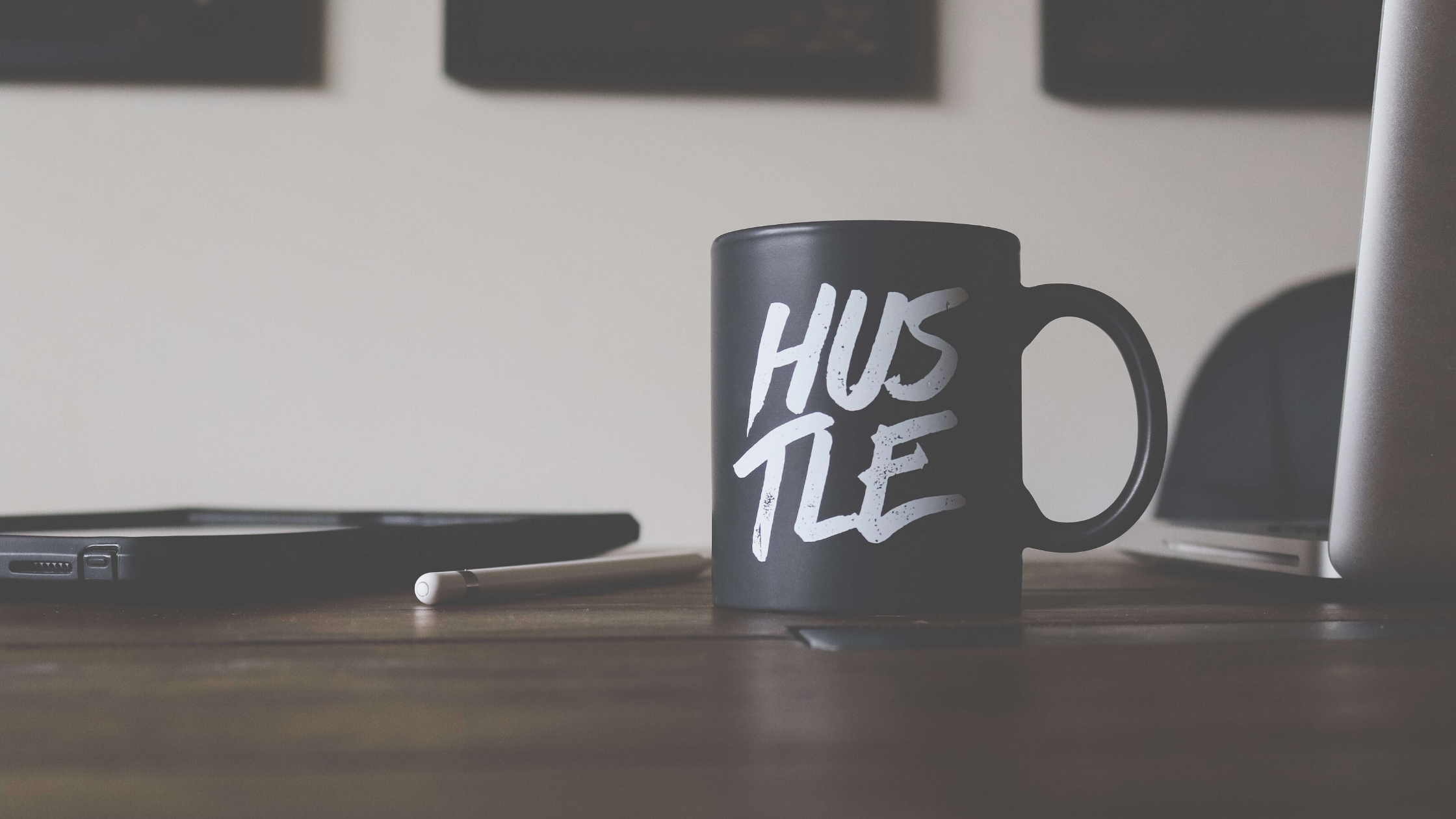 A black mug that says "HUSTLE" in white capital letters sitting on a desk
